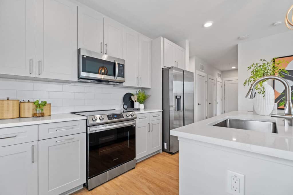 Modern kitchen with white cabinets, stainless steel appliances, a double sink, potted plants, and wood flooring.