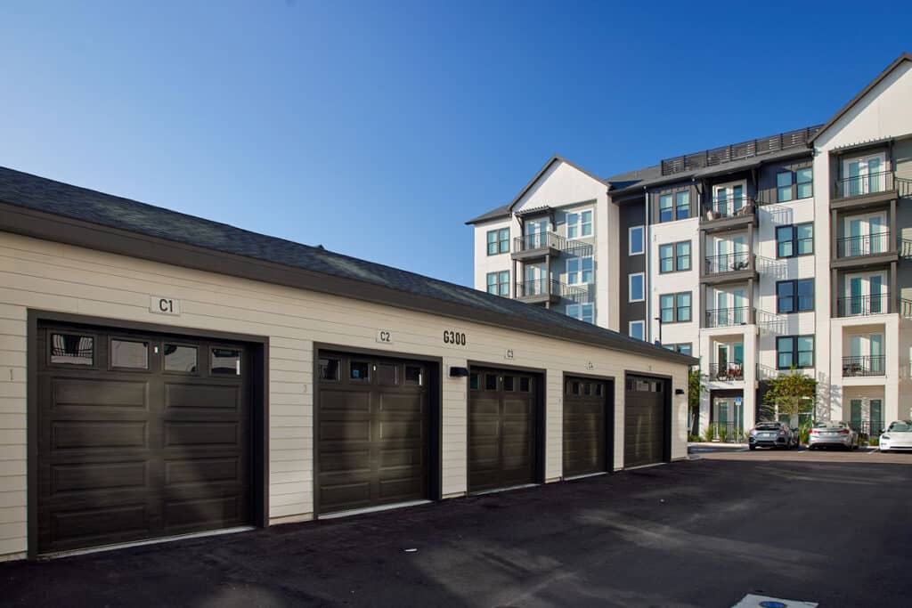 Row of closed garage doors labeled C1 to C6 in front of a modern multi-story apartment building under a clear blue sky.