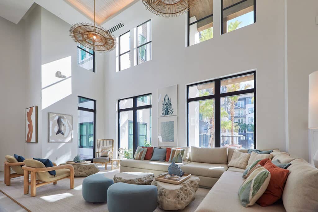 Bright, modern living room with large windows, neutral furniture, blue and beige accents, contemporary art, and natural light streaming in.